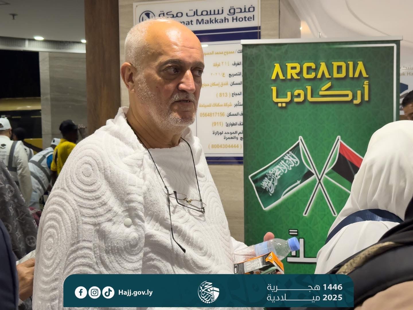 Man in white ihram clothing at Hajj with Arcadia banner
